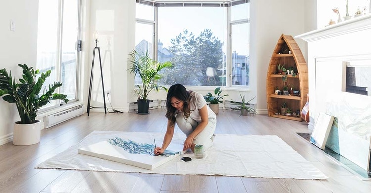 An artist creating on a canvas that is lying on the floor