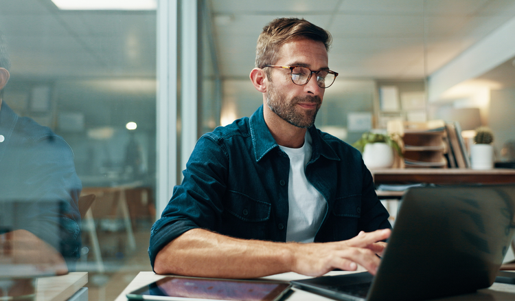 A man sitting at a desk types on his laptop.