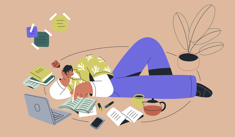 A man with a laptop and books around him writes in a notebook.