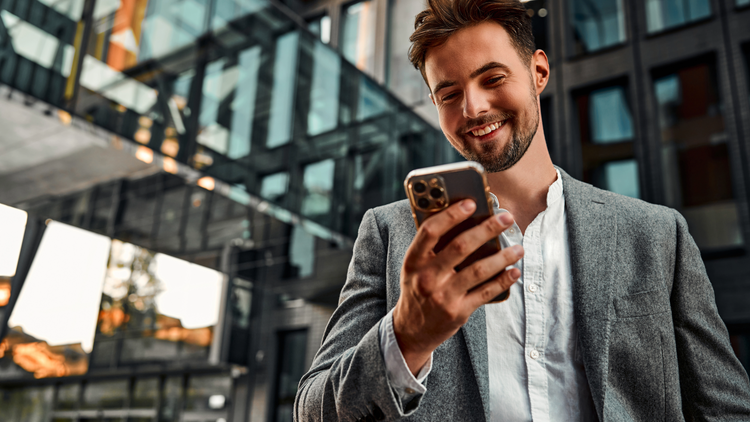 A man stands outside smiling as he looks down at his phone.
