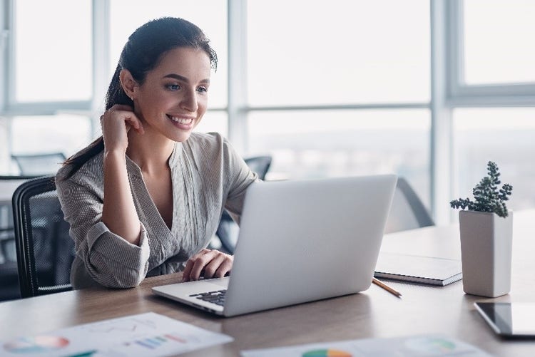 Professional woman smiling and sitting at her laptop.