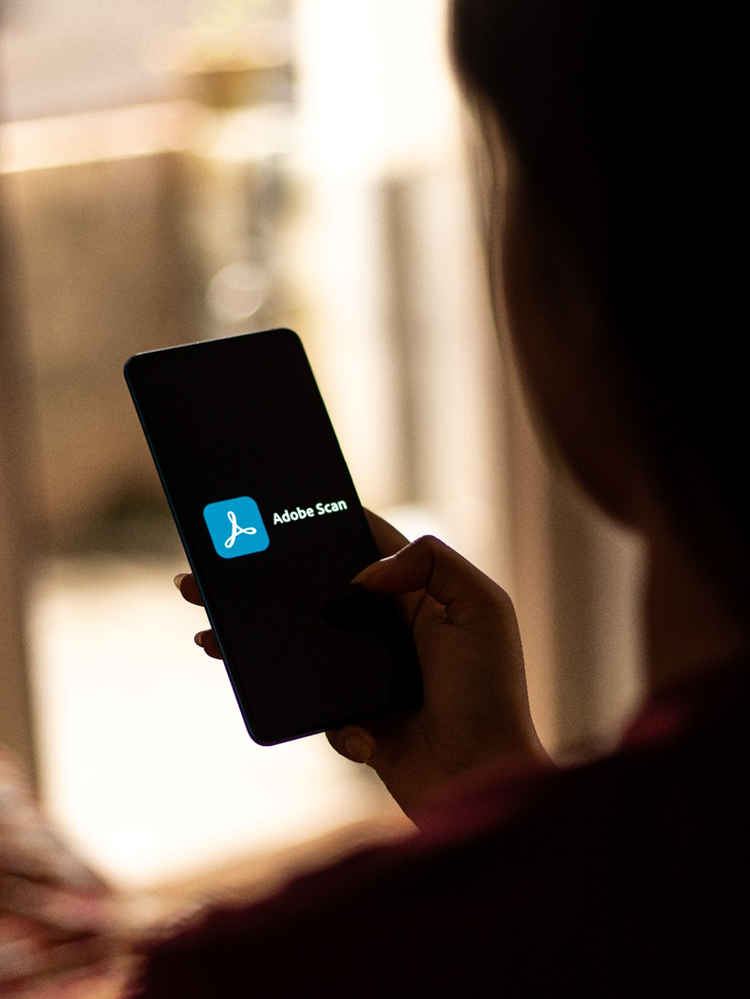 Silhouette of a person holding a mobile phone with the Adobe Scan app logo on the centre of the screen.