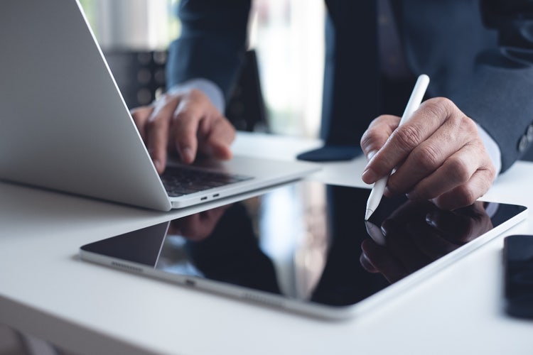 Close-up of a businessman using a digital pen on a digital tablet and using the laptop on an office desk.