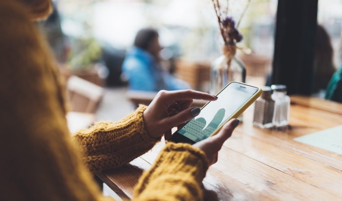 Young professional scrolling on an iPhone in a café.
