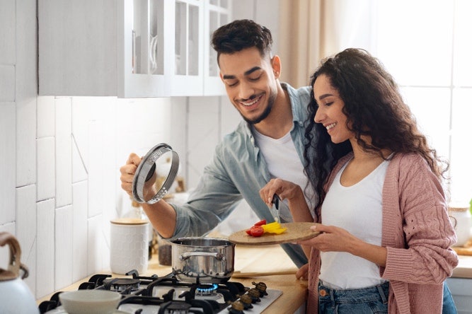 A couple (male and female) cooking in the kitchen, looking into a pot on the hob.