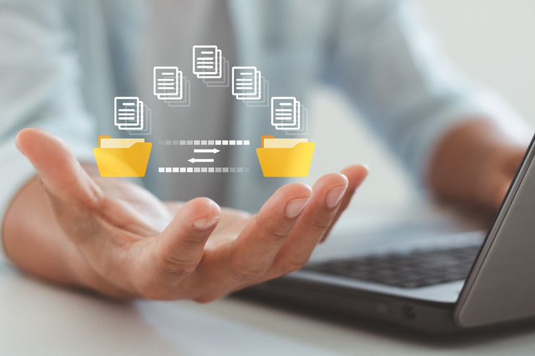 Torso of a person sitting a laptop. A conceptual diagram of digital files being transferred between folders is in the palm of one hand.