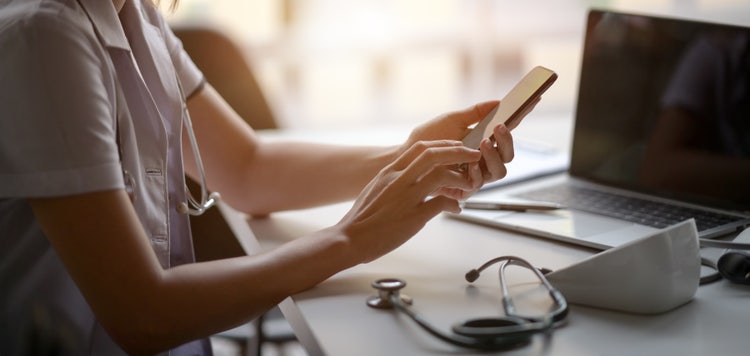 Young female doctor using a smartphone while reviewing medical charts, showcasing mobile accessibility for healthcare documentation.