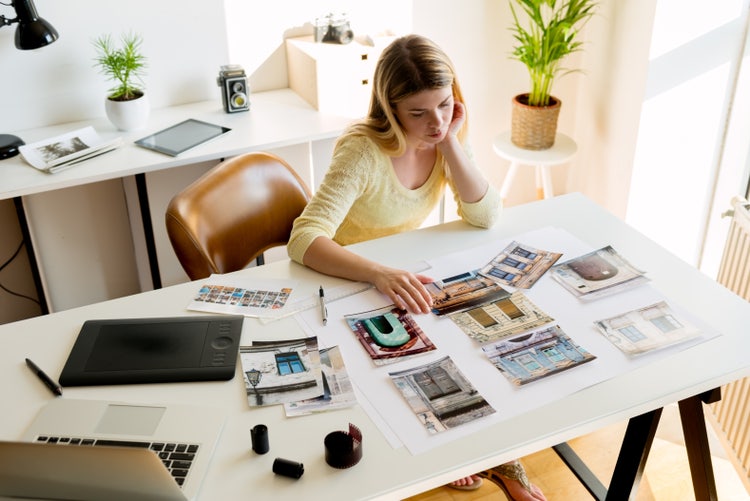 A woman reviewing photos and designs at her desk, working on a creative portfolio.