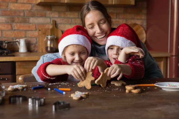 Smiling, loving mother enjoying baking Christmas cookies with her two young children in the kitchen.