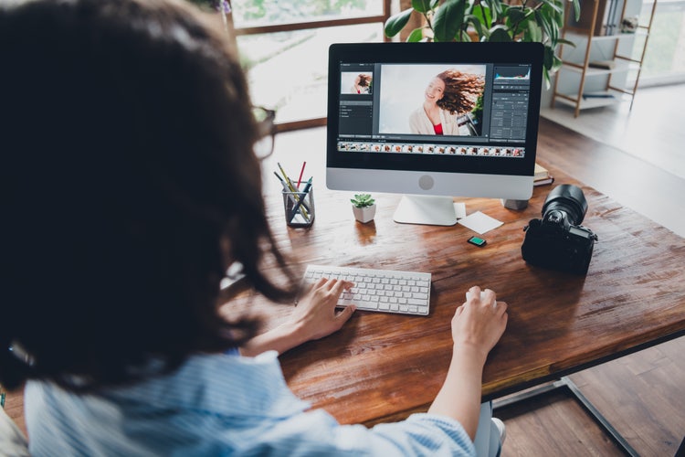 Freelancer editing a portrait using Photoshop on a desktop computer, with a camera and workspace essentials.