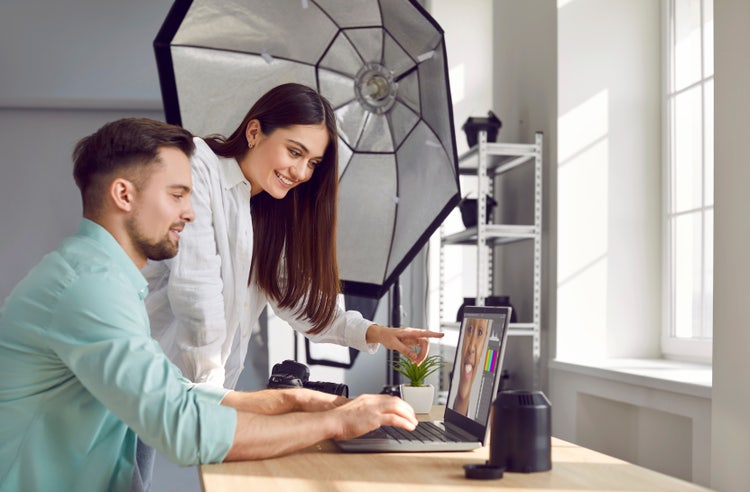 Two photographers collaborating on photo selection using a laptop during a studio photoshoot, focusing on photo editing and retouching.