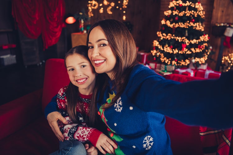 Photo of a mother and daughter sitting on a sofa, taking a selfie in Christmas jumpers.