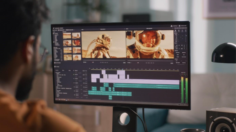 Back view of a video editor in front of a computer, using a video editing software to repurpose long videos to short clips.