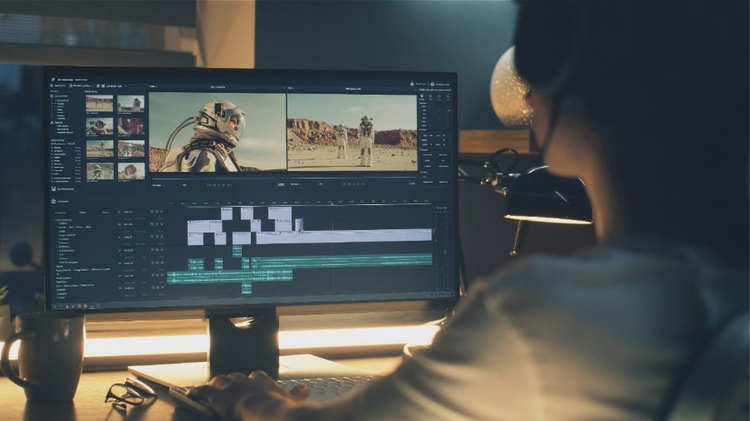 A guy in front of his home-office computer, editing clips using a video editing software.