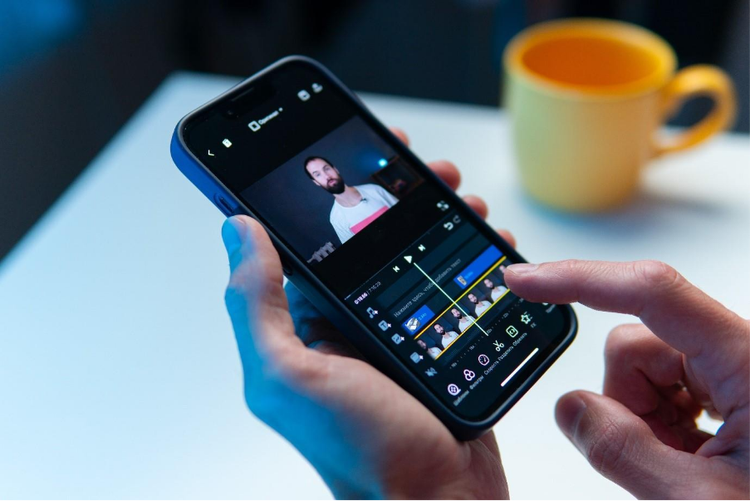 A pair of hands holding a mobile phone and using a video editing app to compress a clip.