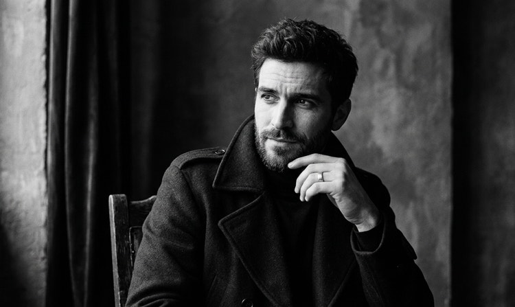 Детайлно черно-бяло генерирано с ИИ изображение на седящ мъж, който гледа замислено към източник на светлина.