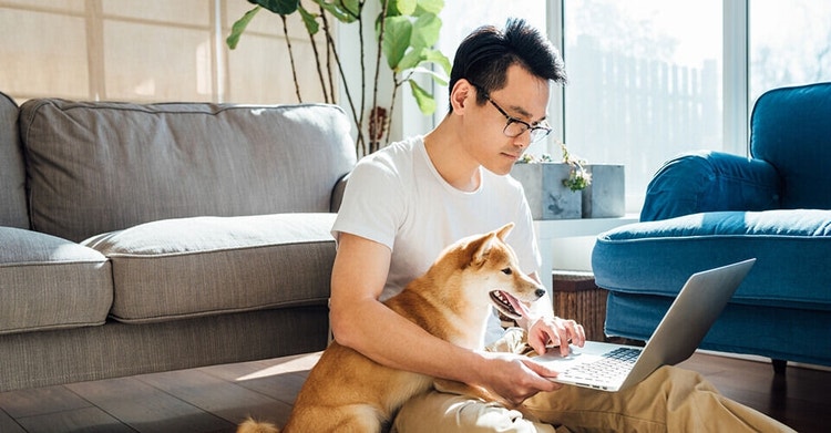 Um homem usando óculos sentado no chão junto com seu cachorro, revisando uma carta de intenção no notebook