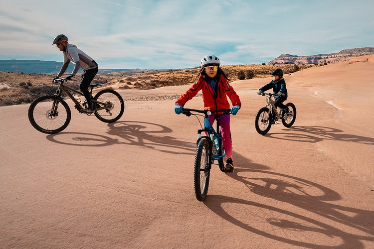 Três pessoas participando de uma excursão escolar, pedalando em mountain bikes no deserto após usar um modelo de autorização editável.