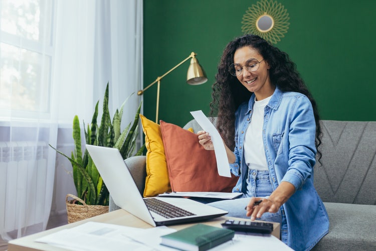 Uma mulher sentada em um sofá aprende a criar um orçamento eficaz com um notebook e uma calculadora.