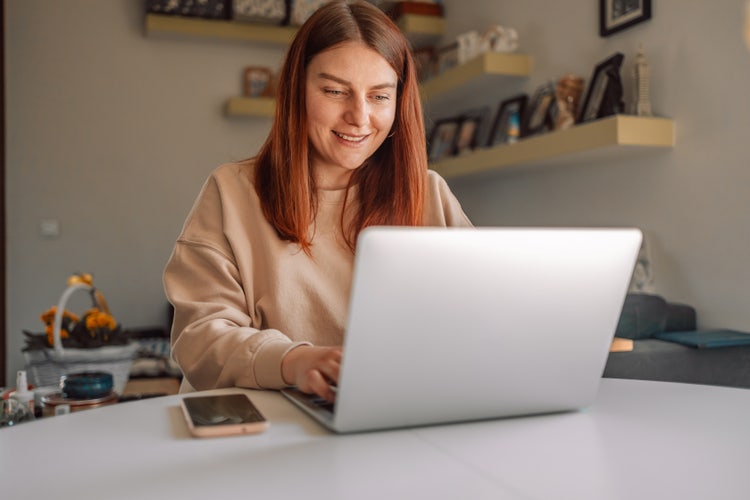 Uma mulher sentada à mesa comprime apresentações do PowerPoint em seu notebook.