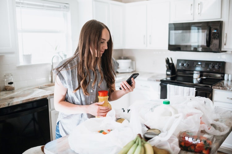 Uma mulher aprende a fazer um orçamento de compras usando o celular na cozinha.