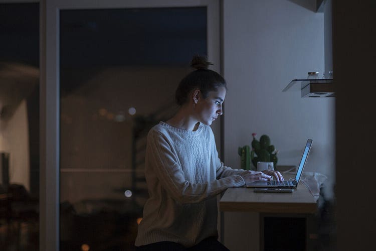 Pessoa elaborando uma carta de interesse no notebook sentada a um balcão de uma cozinha pouco iluminada