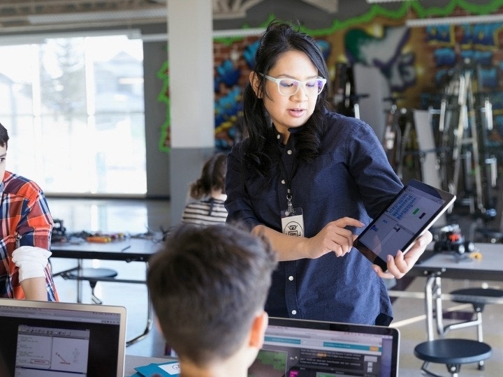Uma professora ministrando enquanto os alunos fazem anotações com cadernos digitais interativos em seus notebooks