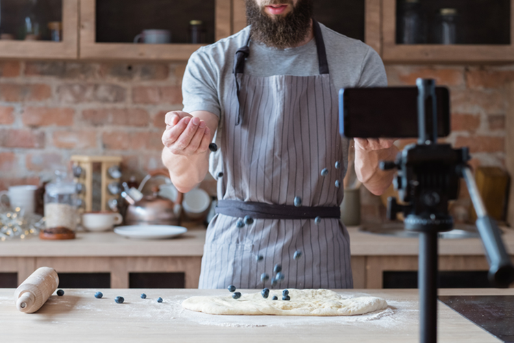 Une personne ajoute des myrtilles à une pâte et enregistre une vidéo sur la cuisine.