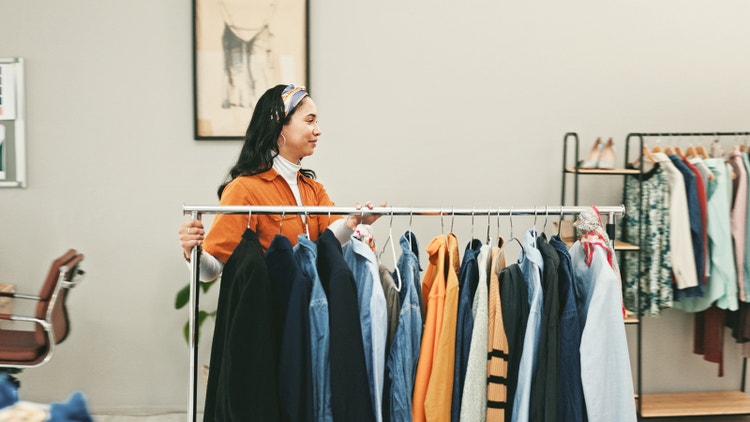 Estilista levando uma arara de roupas.