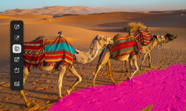 Em uma foto de camelos caminhando no deserto, pegadas em primeiro plano são destacadas para remoção com o pincel no Firefly.