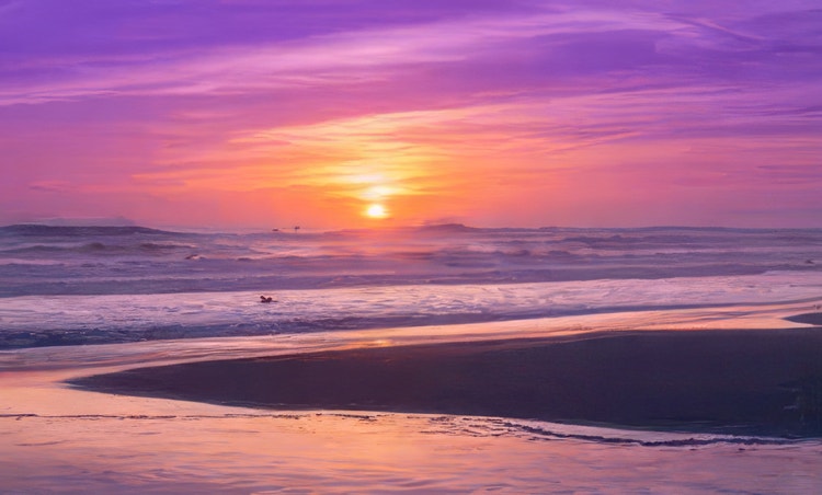 Coucher de soleil sur une plage, illuminant le ciel et les vagues d'une lumière rose et jaune