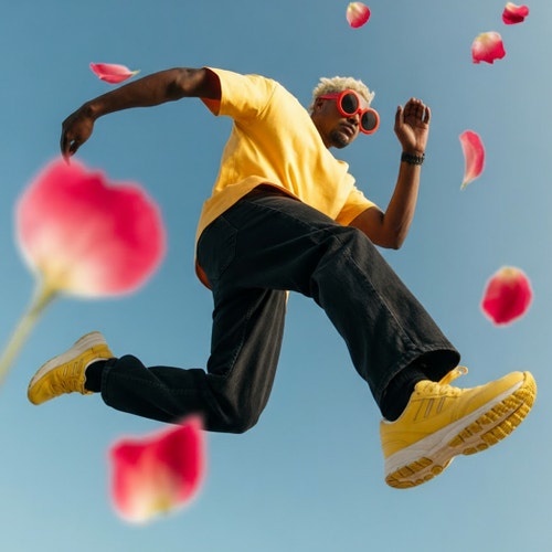 AI generated image created with Ideogram showing a person in yellow shirt and red sunglasses jumping among pink flowers against blue sky.