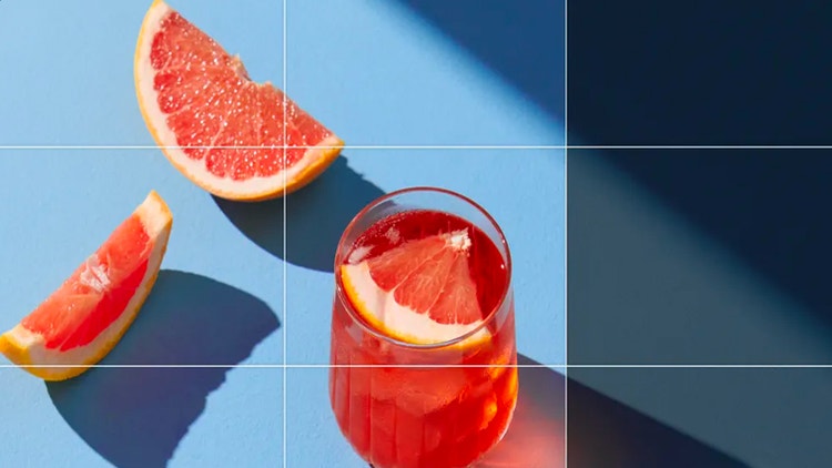 A photo of grapefruit slices next to a pink cocktail is extended to show the full shadow cast by the cocktail glass.