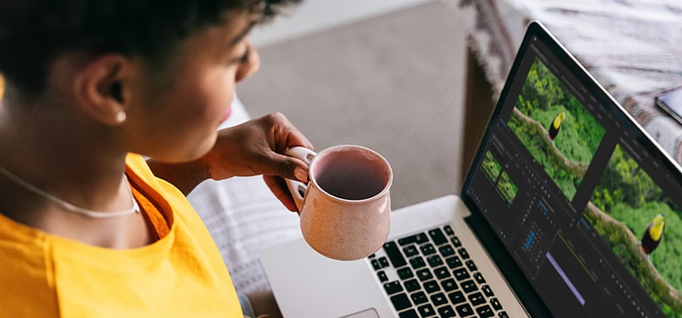 Personne tenant une tasse de café dans une main et transcodant une vidéo dans Adobe {{premiere}} sur son ordinateur portable