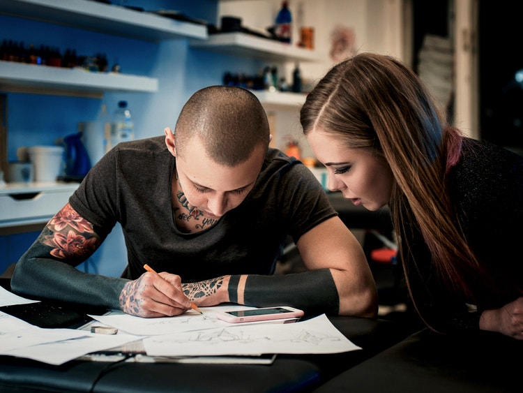 Tatoueur esquissant un croquis sur papier tout en échangeant avec une cliente