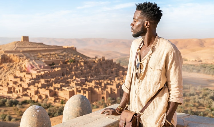 Un uomo osserva un villaggio nel deserto da una sporgenza.