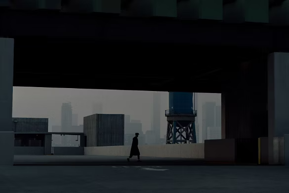An unknown figure shrouded by dark shadows walking across an empty city parking garage