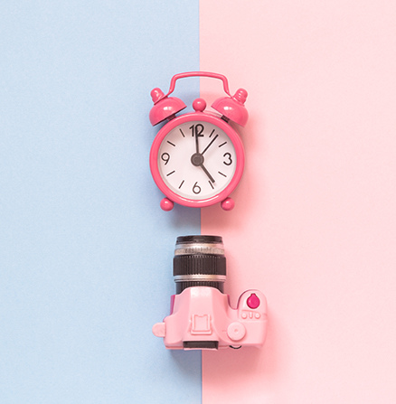 Still-life capture of a pink analog alarm clock above a pink digital camera