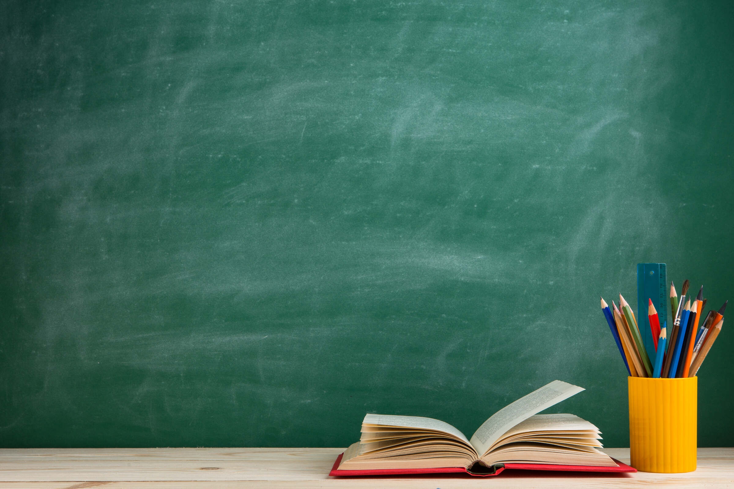 Un livre et un pot de crayons devant un tableau vert