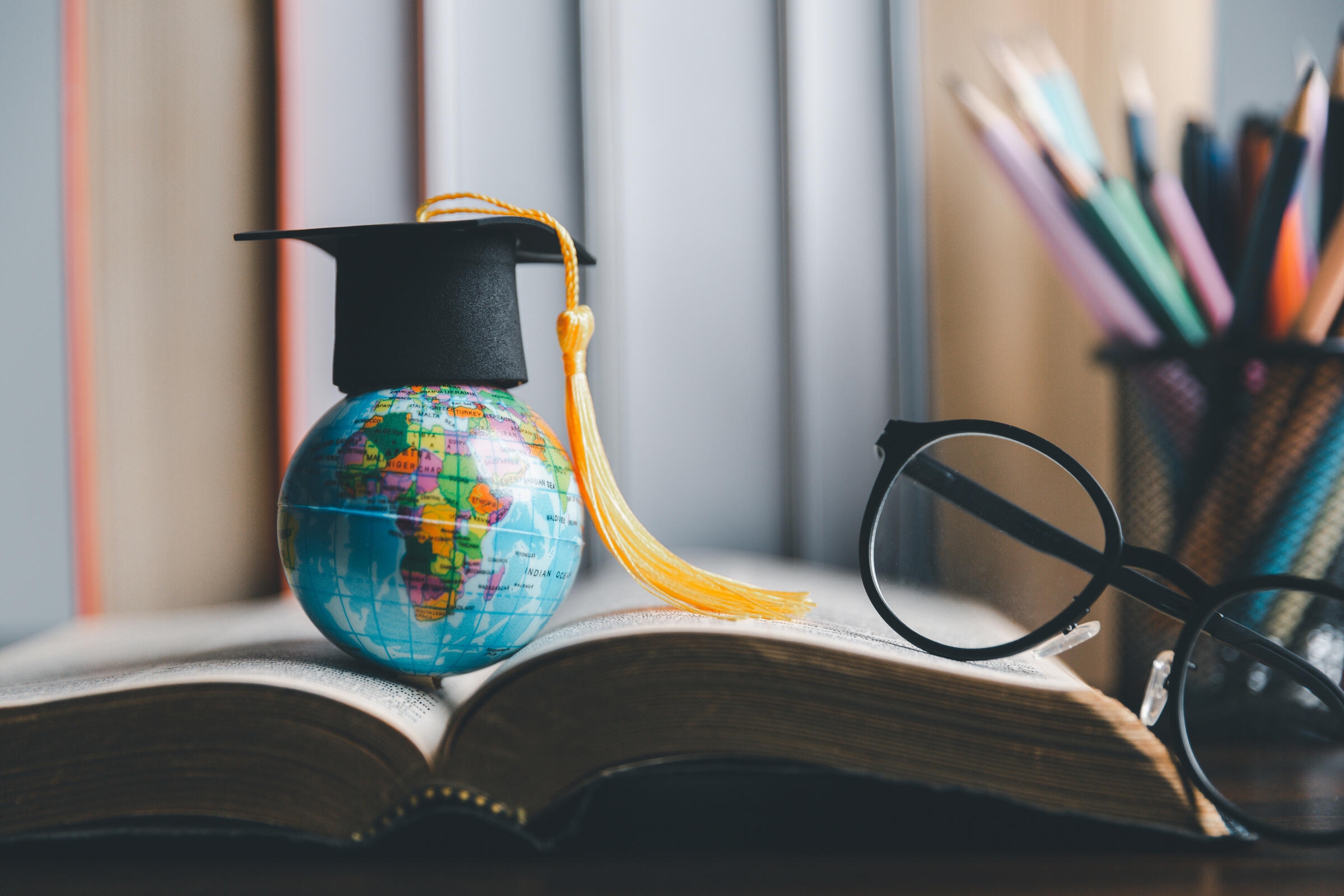 Un motarboard et un globe posés sur un livre d'étudiant