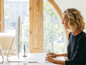 Side view of a woman sitting at a shared desk in front of an iMac