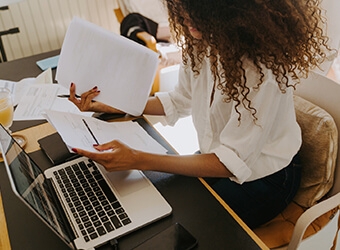 A person sitting at a desk with their laptop and reviewing paper documents
