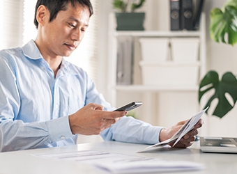 A person sitting at a desk and checking their phone while reviewing a document