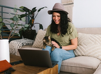 A person with a cat in their lap sitting on a couch while looking at their laptop computer