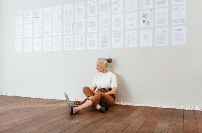 Woman sitting on floor with a laptop in front of a wall with printed papers taped to it