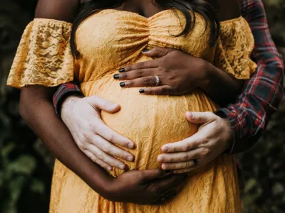 A close-up maternity photo of a couple embracing with their hands framing the stomach.