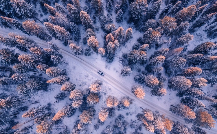 An aerial view of a car driving on a snowy forest road with an Open in Premiere UI overlay.