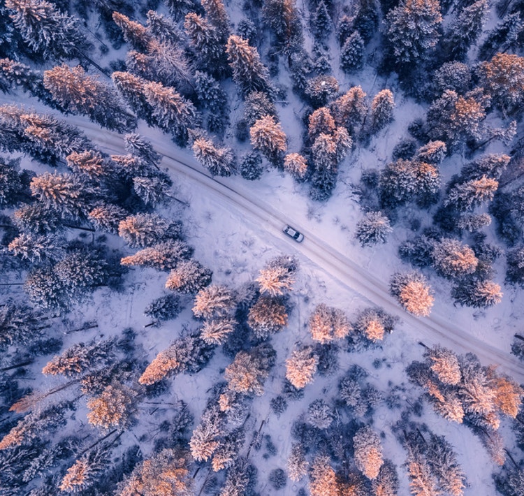 An aerial view of a car driving on a snowy forest road with an Open in Premiere UI overlay.