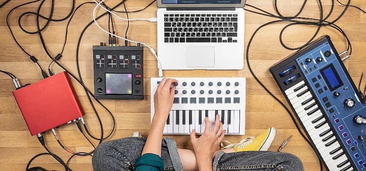 Frau produziert mit Keyboard, Synthesizer und Laptop Musik im Homestudio.