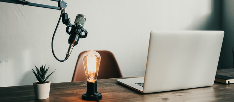 Podcast-Arbeitsplatz mit Mikrofon, Laptop und leuchtender Vintage-Lampe auf einem Schreibtisch.